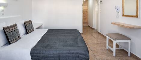 A bedroom with a bed, bedside lamp, wall-mounted mirror, and a bench.