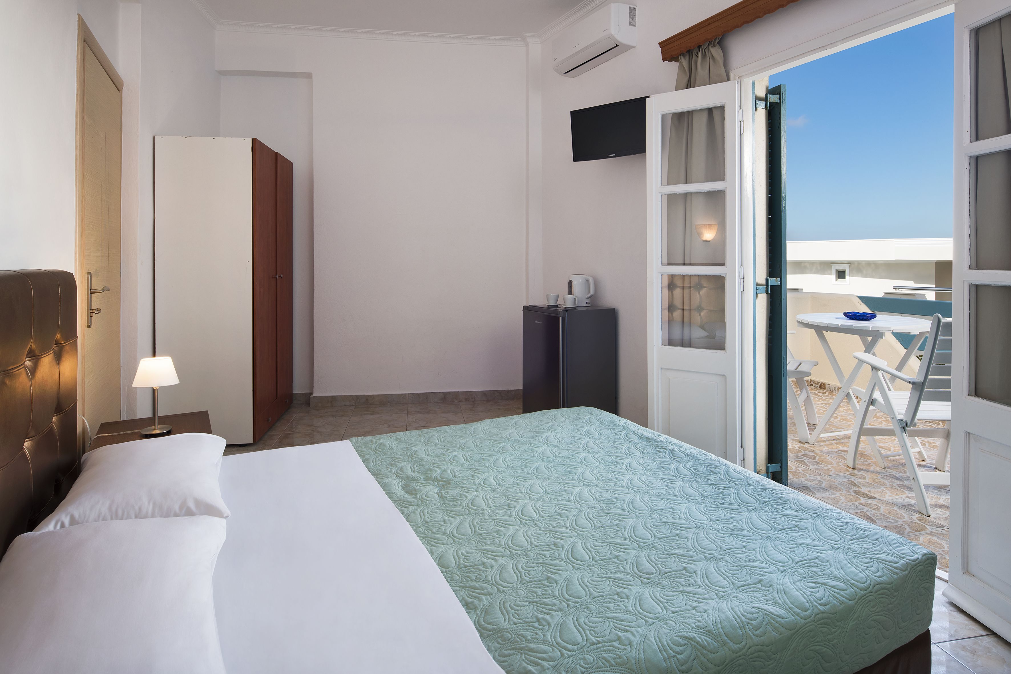 Une chambre d’hôtel comprenant un lit, un bureau, une chaise, une télévision et un balcon avec une table et des chaises.