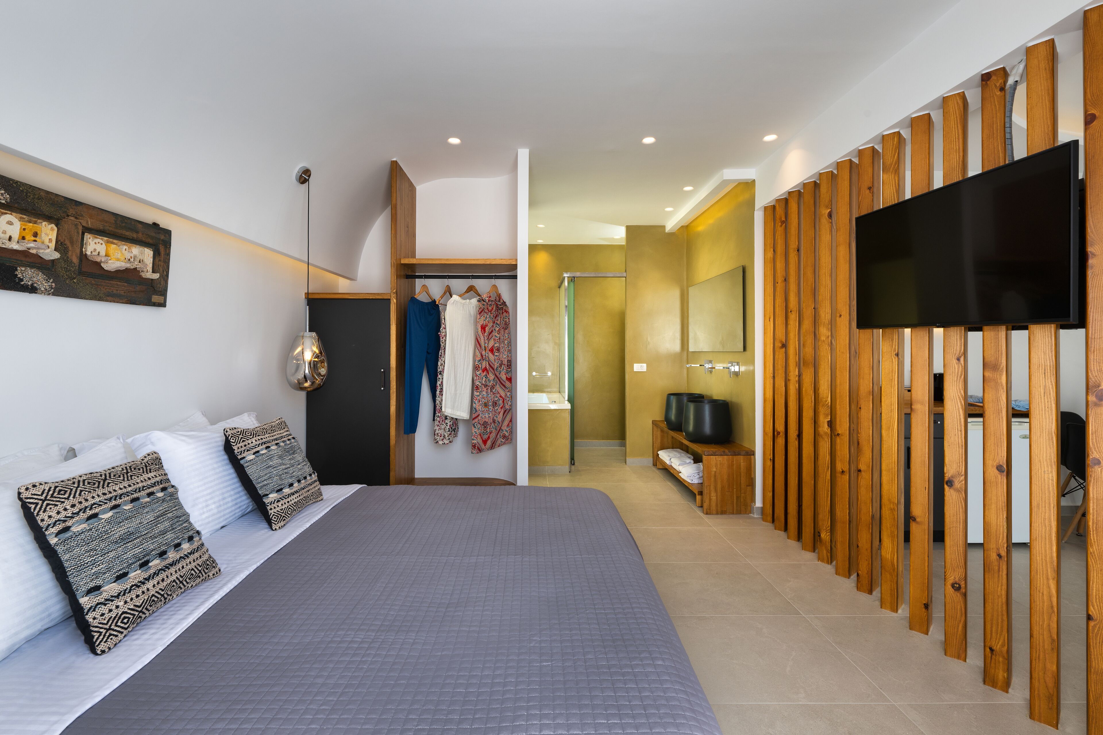 A modern bedroom with a large bed, a wooden partition, a TV, and a bathroom visible in the background.