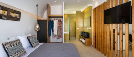 A modern bedroom with a large bed, a wooden partition, a TV, and a bathroom visible in the background.