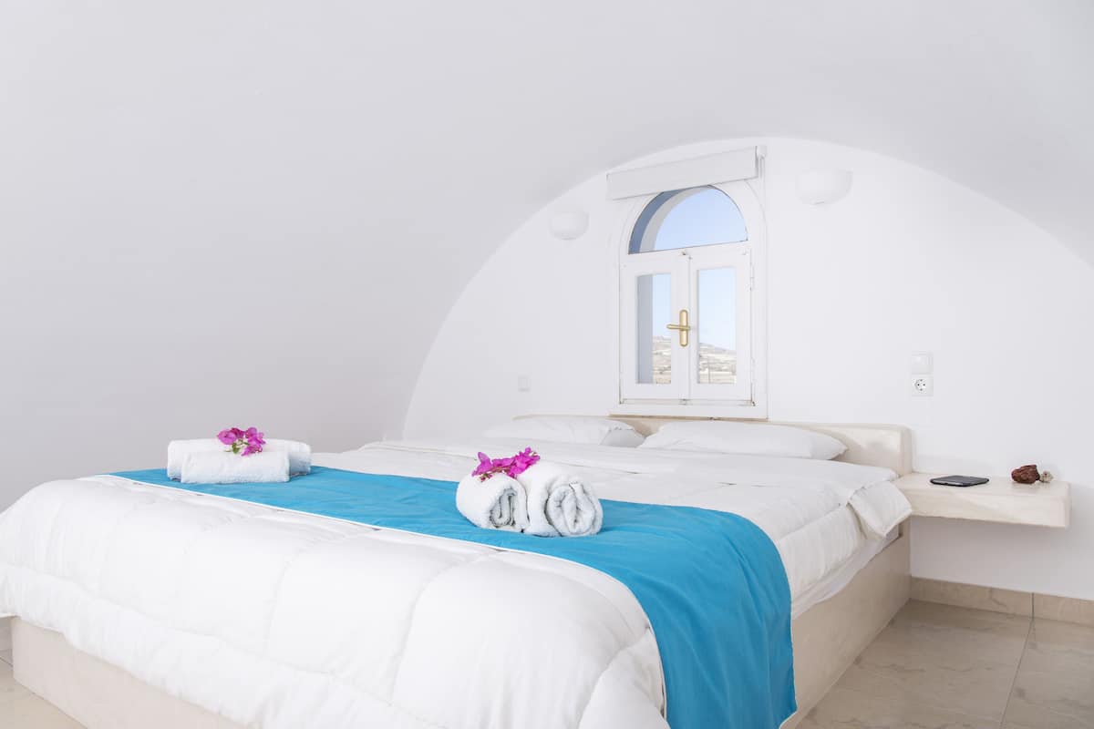 A bedroom with a bed, a window, and a bedside table.
