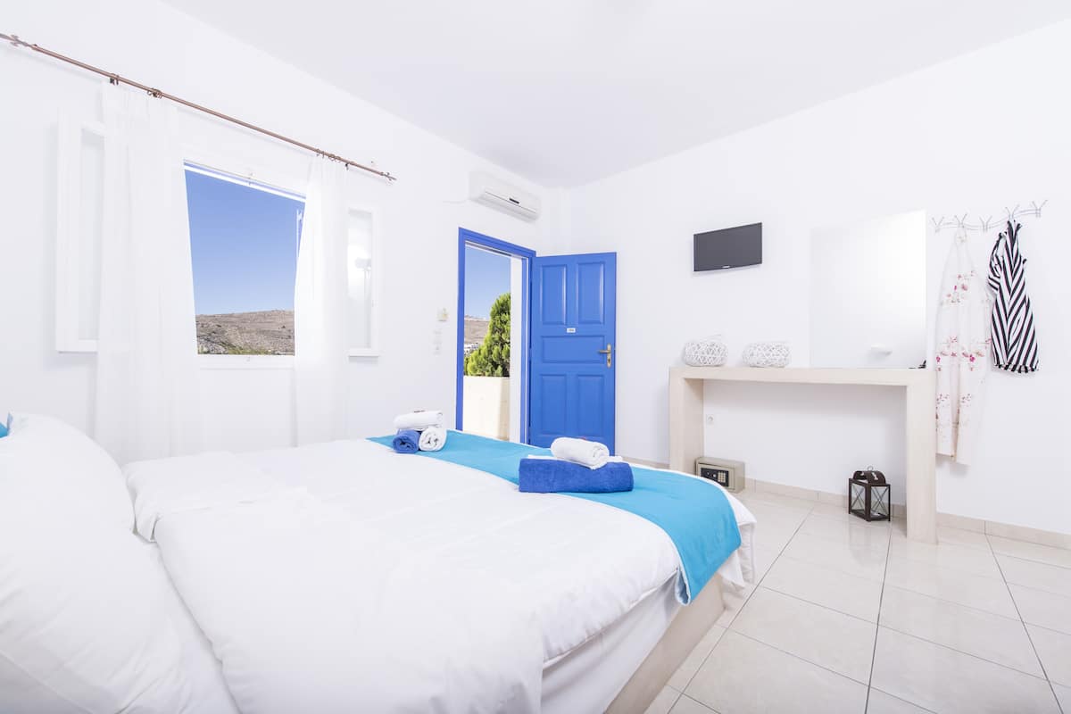 A hotel room with a bed, a blue door, a TV, and a window with a view of the landscape.