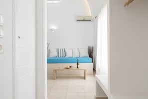 Un intérieur moderne avec une porte blanche, un canapé bleu agrémenté de coussins, une table basse en bois et un appareil de climatisation fixé au mur.