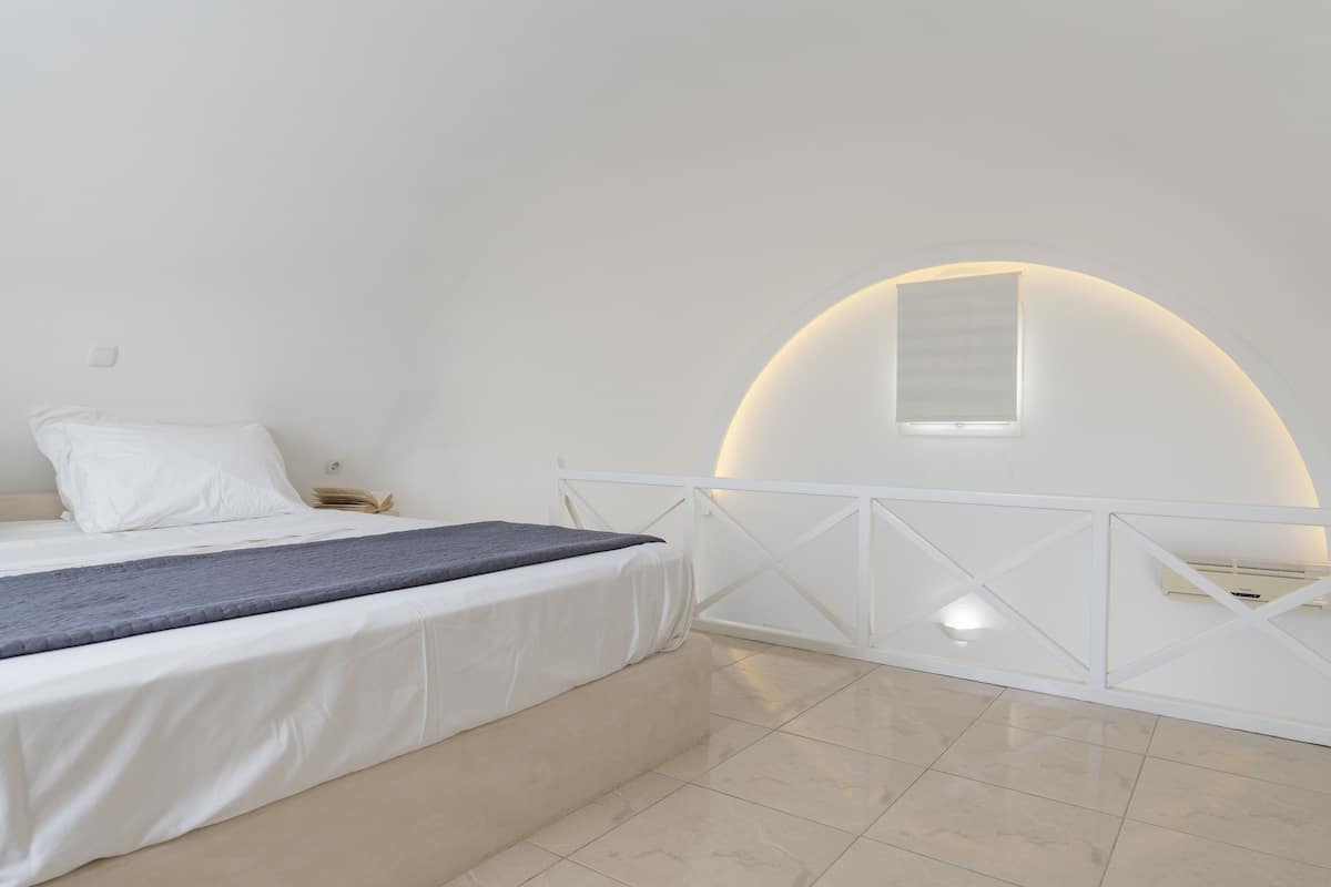 A bedroom with a bed, a nightstand, a bedside table, a window, and a white railing.