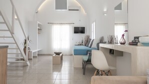 A modern living room with a staircase, a blue sofa, a white chair, and a flat-screen TV mounted on the wall. - Bella Santorini (Santorini)