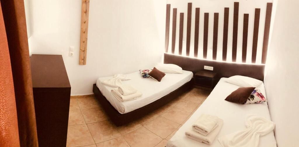 A hotel room with two single beds, a wooden headboard, a small bedside table, and a built-in shelf.
