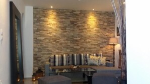 Uma sala de estar moderna com parede de pedra, um sofá, duas poltronas e uma mesa de centro.
