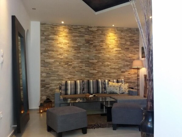 A modern living room with a stone wall, a sofa, two armchairs, and a coffee table. - Villa Livadaros (Santorini)
