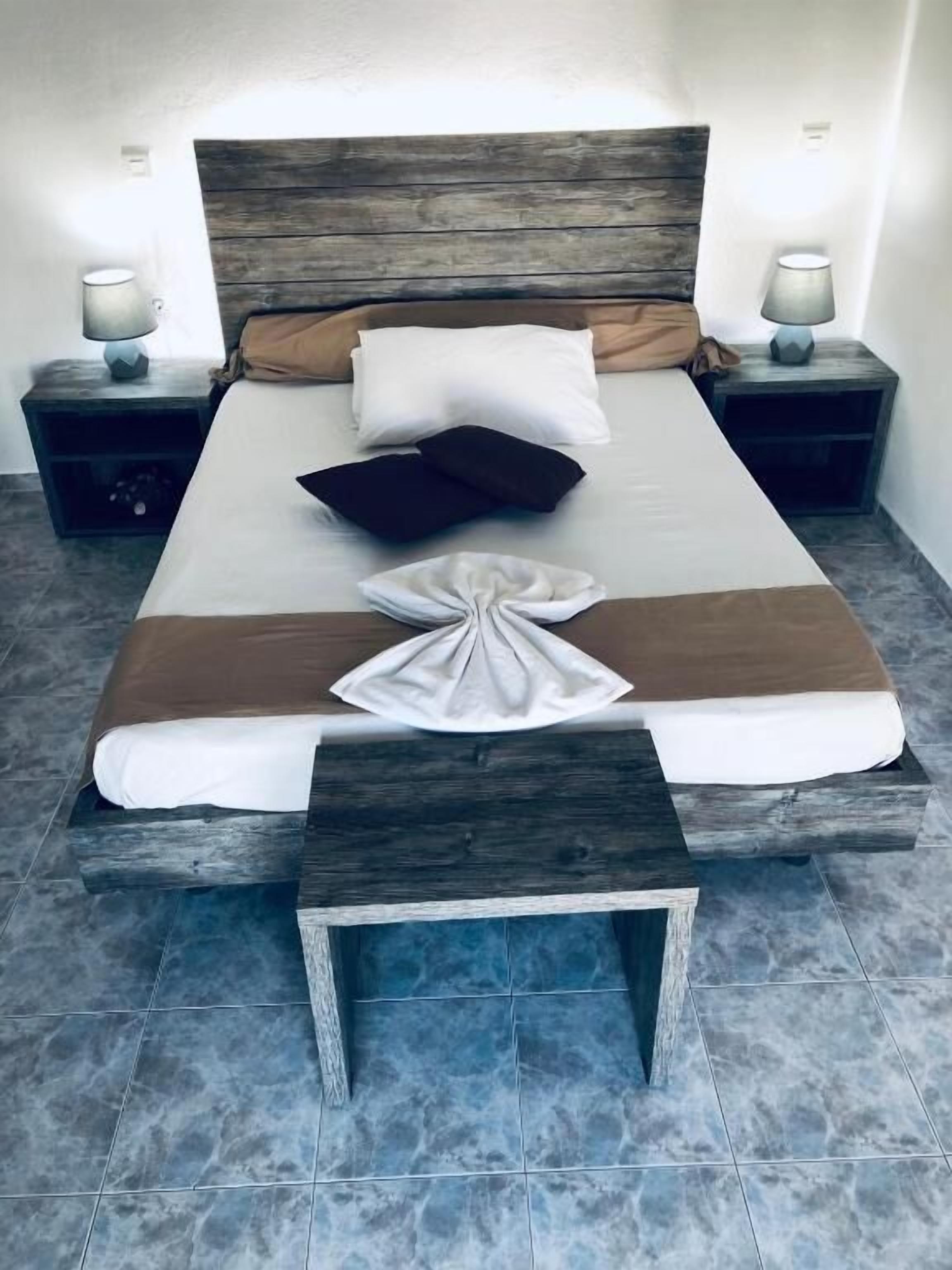 Una cama con cabecera de madera, dos mesitas de noche con lámparas y una toalla decorativa sobre la cama.