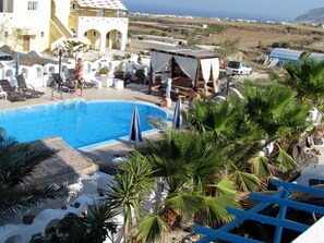 A pool area with lounge chairs, umbrellas, and palm trees. - Villa Livadaros (Santorini)