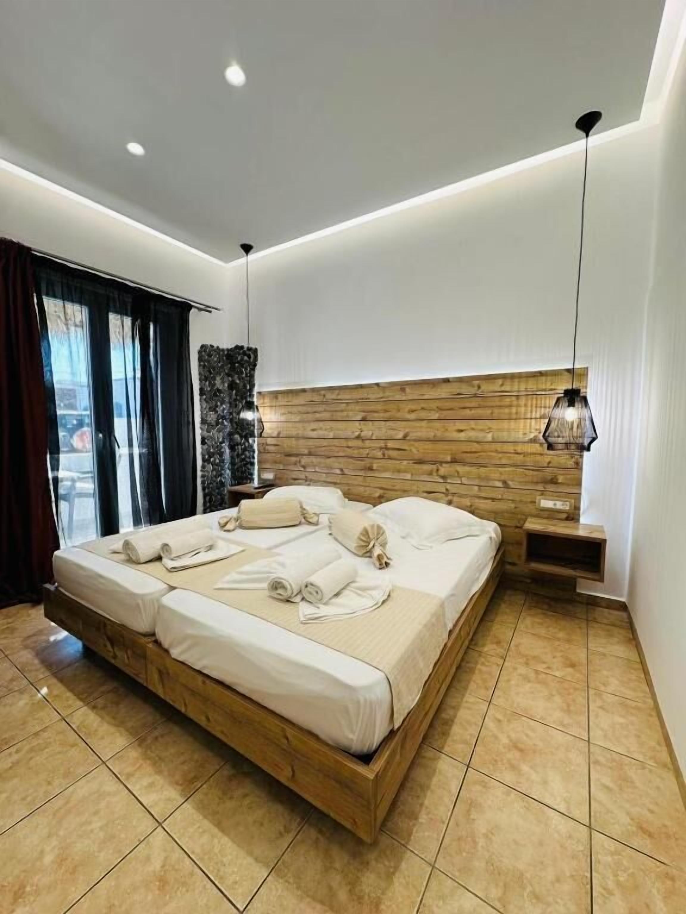 A modern bedroom with a wooden headboard, a large bed with neatly arranged towels, and a hanging pendant light.