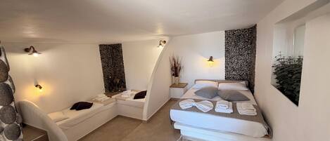 A spa room with a massage table, a small seating area with towels, and a stone wall.