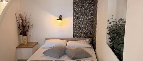 Un lit bien fait, avec des oreillers et des serviettes, un luminaire fixé au mur et un panneau décoratif mural.
