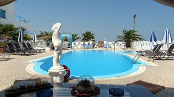 Relax by the serene pool surrounded by lounge chairs and umbrellas, featuring a beautiful statue in the center.