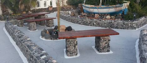 Un espacio al aire libre con paredes de piedra, bancos, un bote y una palmera.