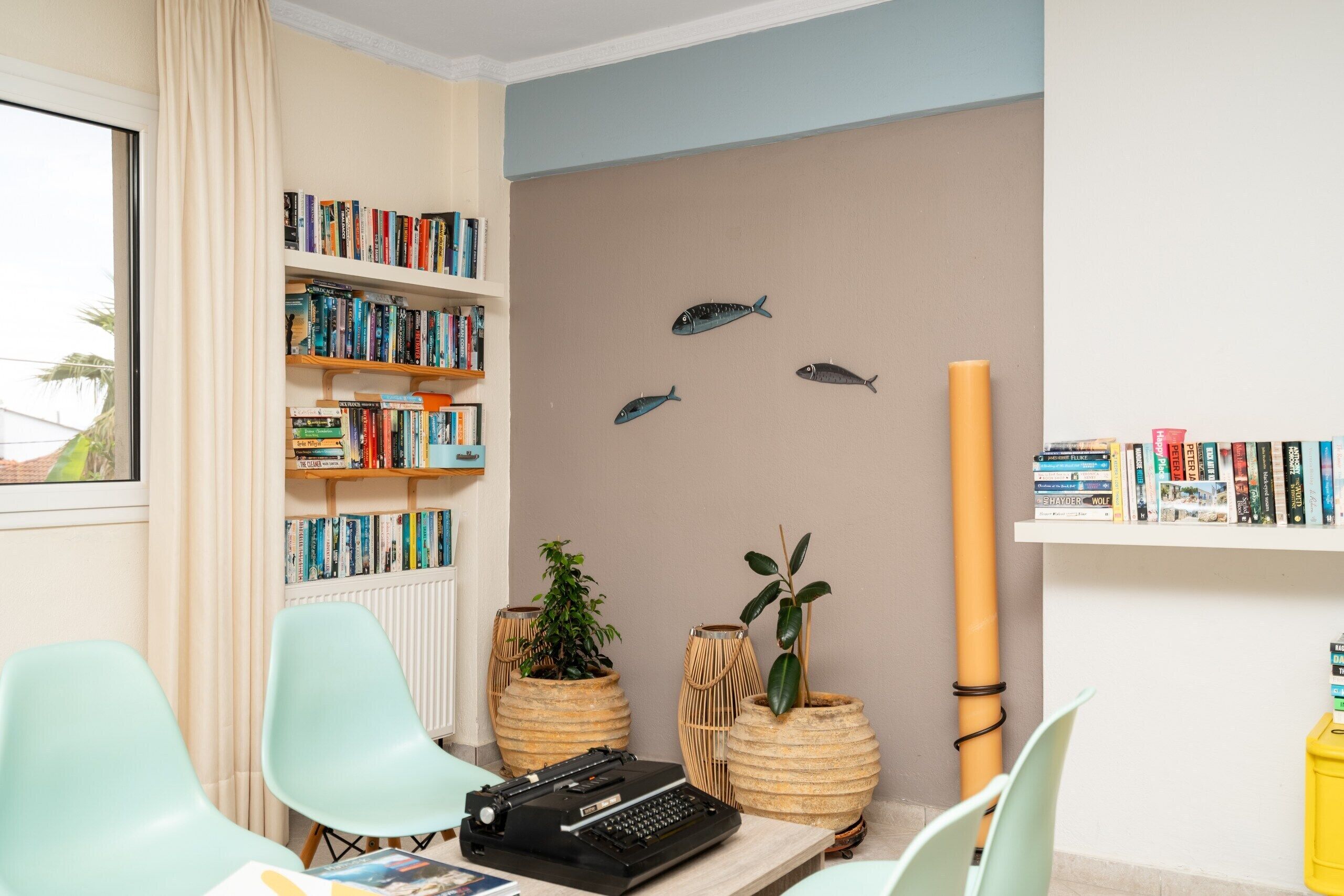 A room with a bookshelf, two chairs, a typewriter, and decorative fish on the wall.