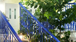Una escalera con barandillas azules y peldaños blancos, rodeada de follaje e iluminada por faroles.