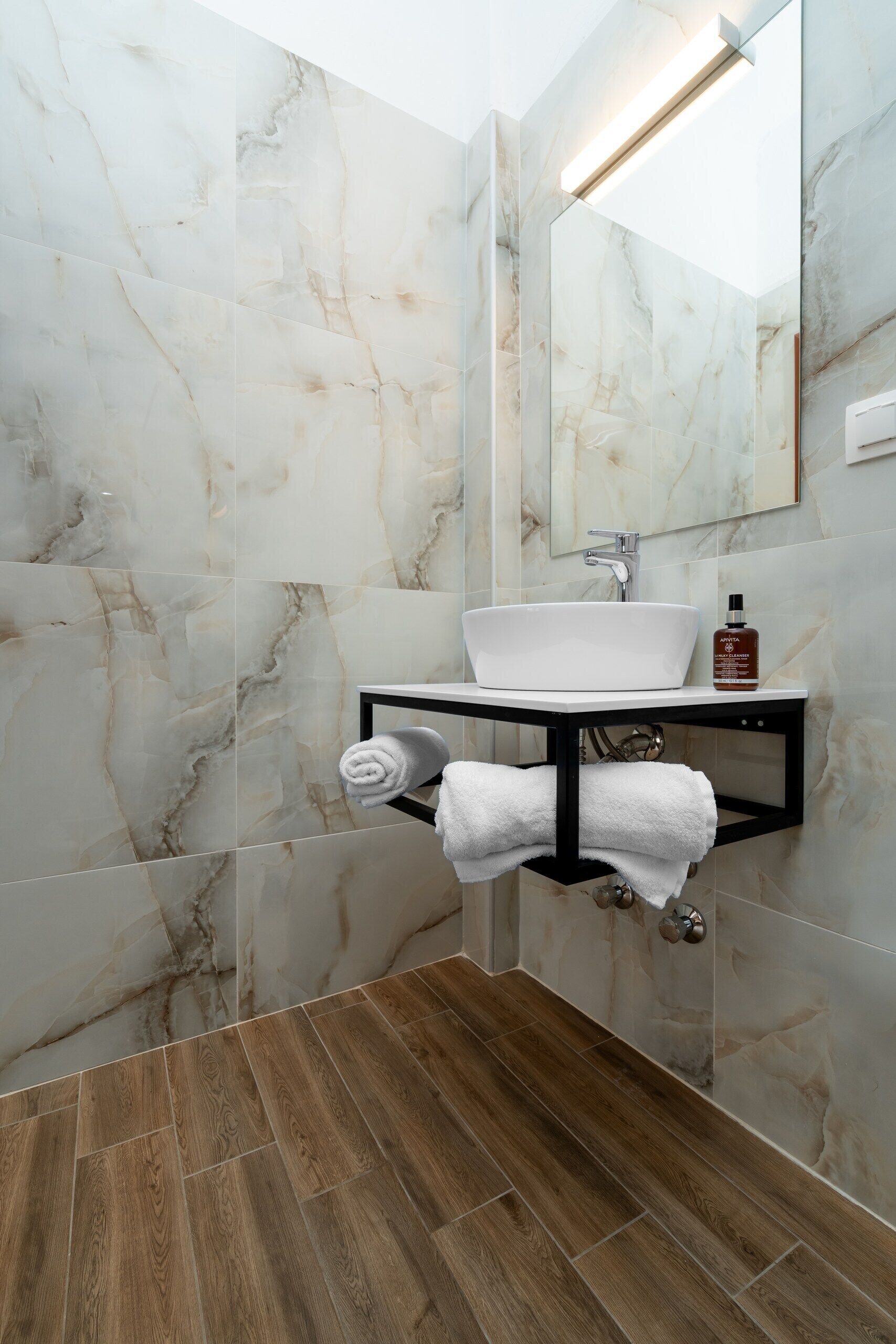 A bathroom with a white sink, black countertop, and marble walls.