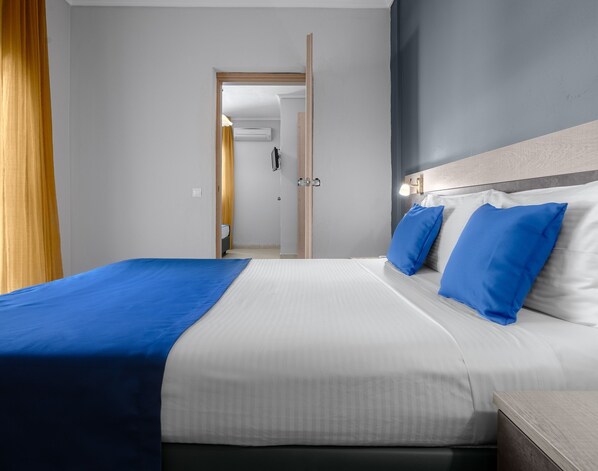 A hotel room with a bed, a nightstand, a lamp, and a door leading to a bathroom.