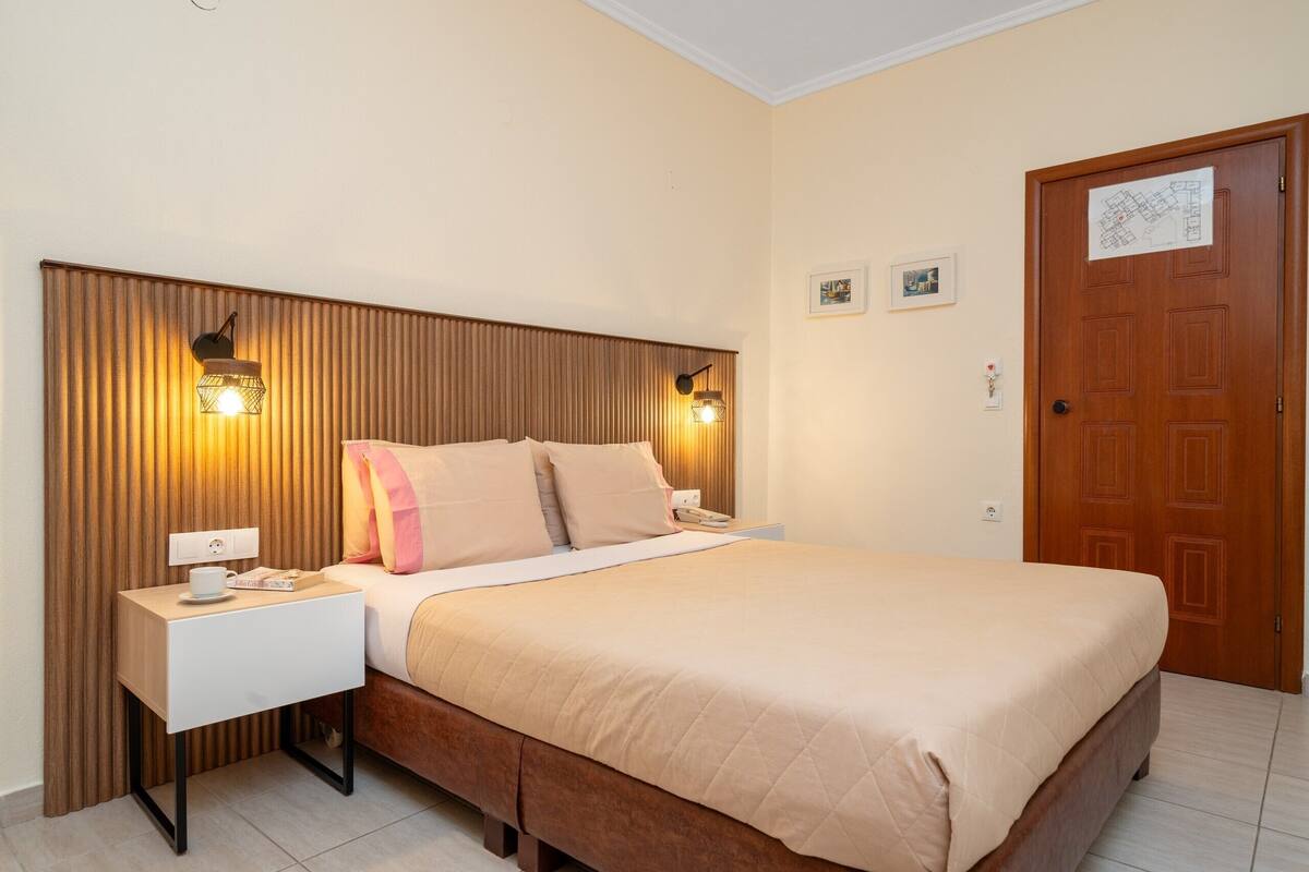 A bedroom with a bed, bedside tables, a wooden headboard, wall-mounted lights, a door with a map, and a small picture on the wall.