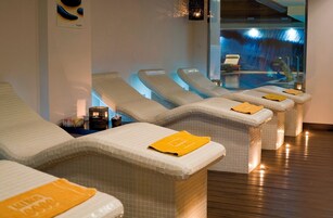 Filas de tumbonas de spa con toallas, suelo de madera y vistas a una piscina interior.
