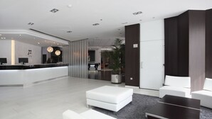 A modern hotel lobby with a reception desk, white sofas, a dark coffee table, and a large potted plant. - Hotel & Spa Villa Olímpic@ Suites (Barcelona)