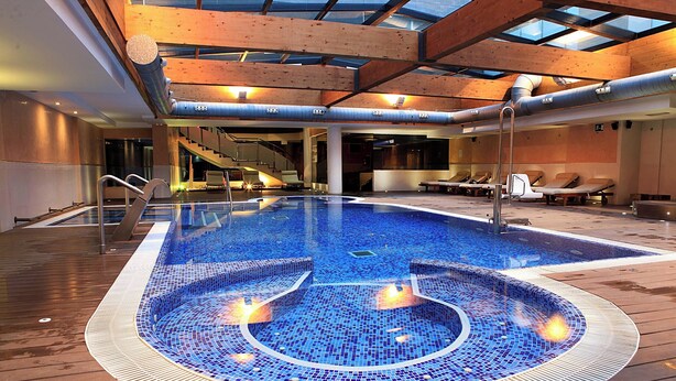 An indoor swimming pool with a wooden deck, lounge chairs, and a glass ceiling. - Hotel & Spa Villa Olímpic@ Suites (Barcelona)