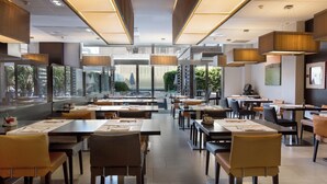 A spacious restaurant with high ceilings, modern lighting, and large windows offering views of greenery. - Hotel & Spa Villa Olímpic@ Suites (Barcelona)
