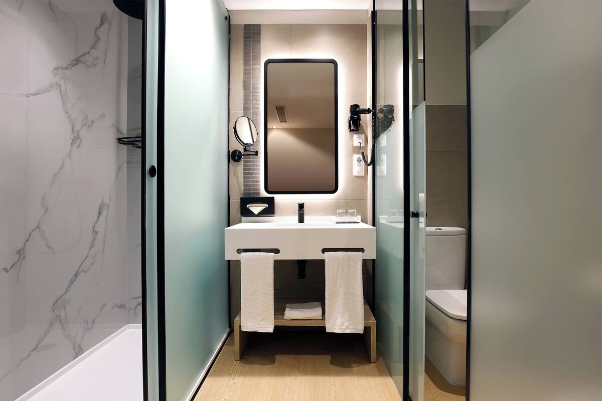 Ein modernes Badezimmer mit Marmorwand, einer Duschkabine aus Glas und einem weißen Waschbecken mit Spiegel darüber.