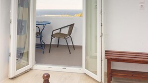 Una habitación con una cama, un televisor montado en la pared y una puerta abierta que da a un balcón con una mesa y sillas.