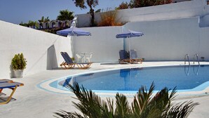 Una piscina con sillas de descanso y sombrillas, rodeada por un muro blanco y plantas en macetas.