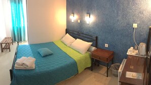 Un dormitorio con una cama, una mesita de noche, un banco de madera y un escritorio con un teléfono y un cubo de basura.