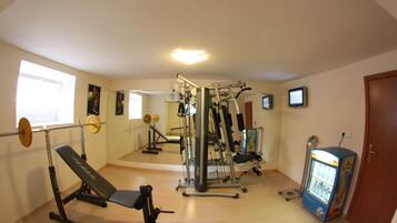 Ein Fitnessraum mit Trainingsgeräten, einer Bank, einem Gewichtsständer und einem Getränkeautomaten.
