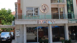 Ein mehrstöckiges Hotel mit einem großen Schild mit der Aufschrift 'ITALY', Balkonen und einem Glas Eingang.