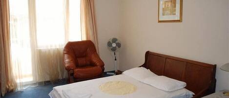 Een hotelkamer met een bed, een stoel, een ventilator en een raam met gordijnen.