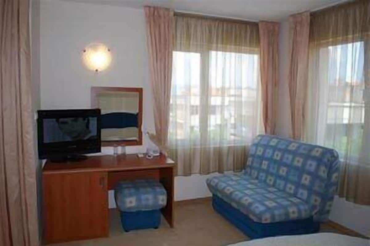 A hotel room with a bed, a desk with a television, a chair, and a window with curtains.