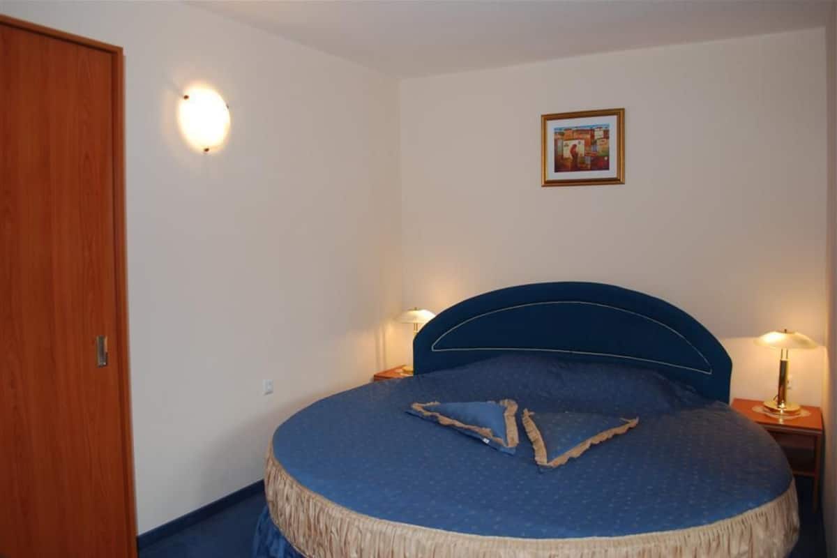 A bedroom with a bed, bedside lamps, a framed picture on the wall, and a wooden door.