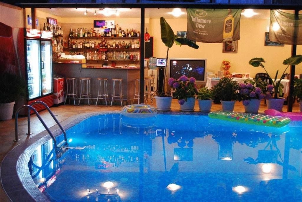 Un área de piscina interior con un bar y zona de estar, rodeada de plantas en macetas.