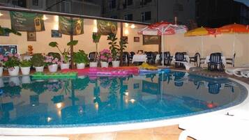An indoor swimming pool with potted plants and umbrellas.