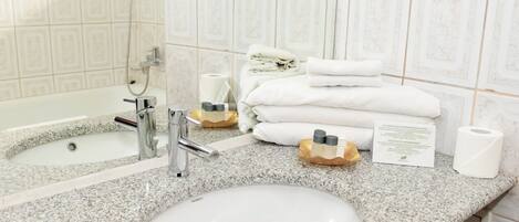 A bathroom with a granite countertop, a sink, a shower, and neatly stacked towels.