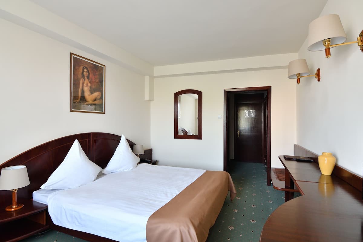 A hotel room with a bed, bedside table, lamp, and a painting on the wall.