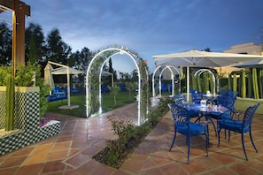 An outdoor patio area with a tiled floor, blue metal chairs, a round table, and white umbrellas providing shade. - Majeka House Boutique Hotel (Stellenbosch)