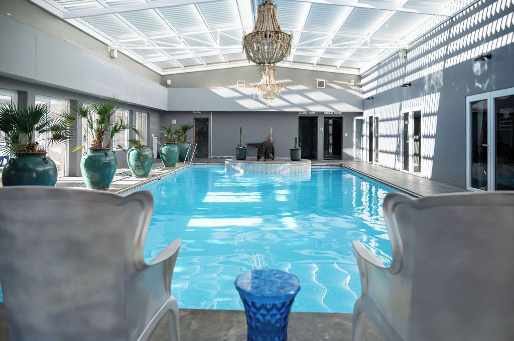 Une piscine intérieure à l’eau d’un bleu limpide, entourée de grands pots de plantes et de chaises modernes.