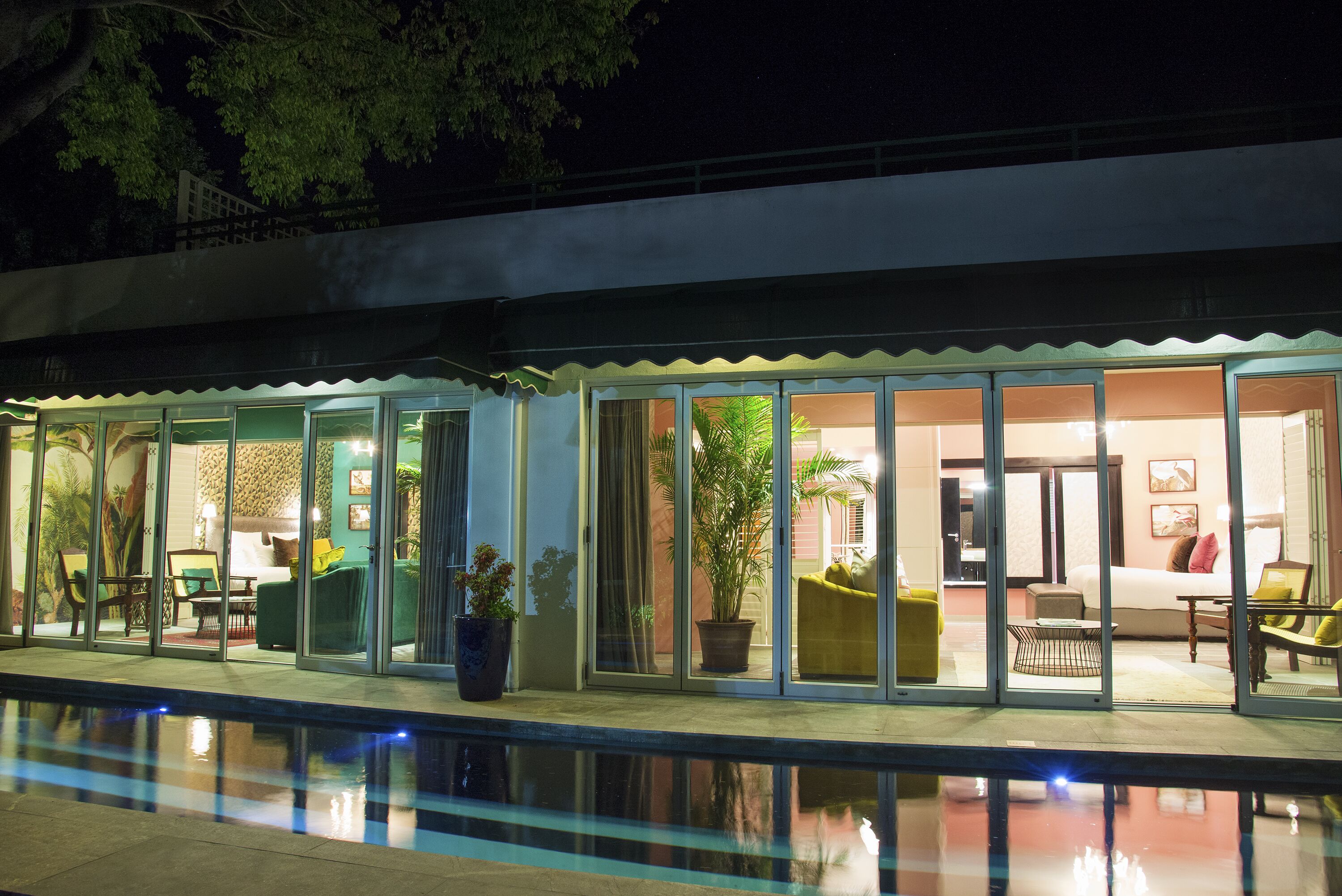 A modern hotel with a pool, glass doors, and a well-lit interior with furniture and plants.