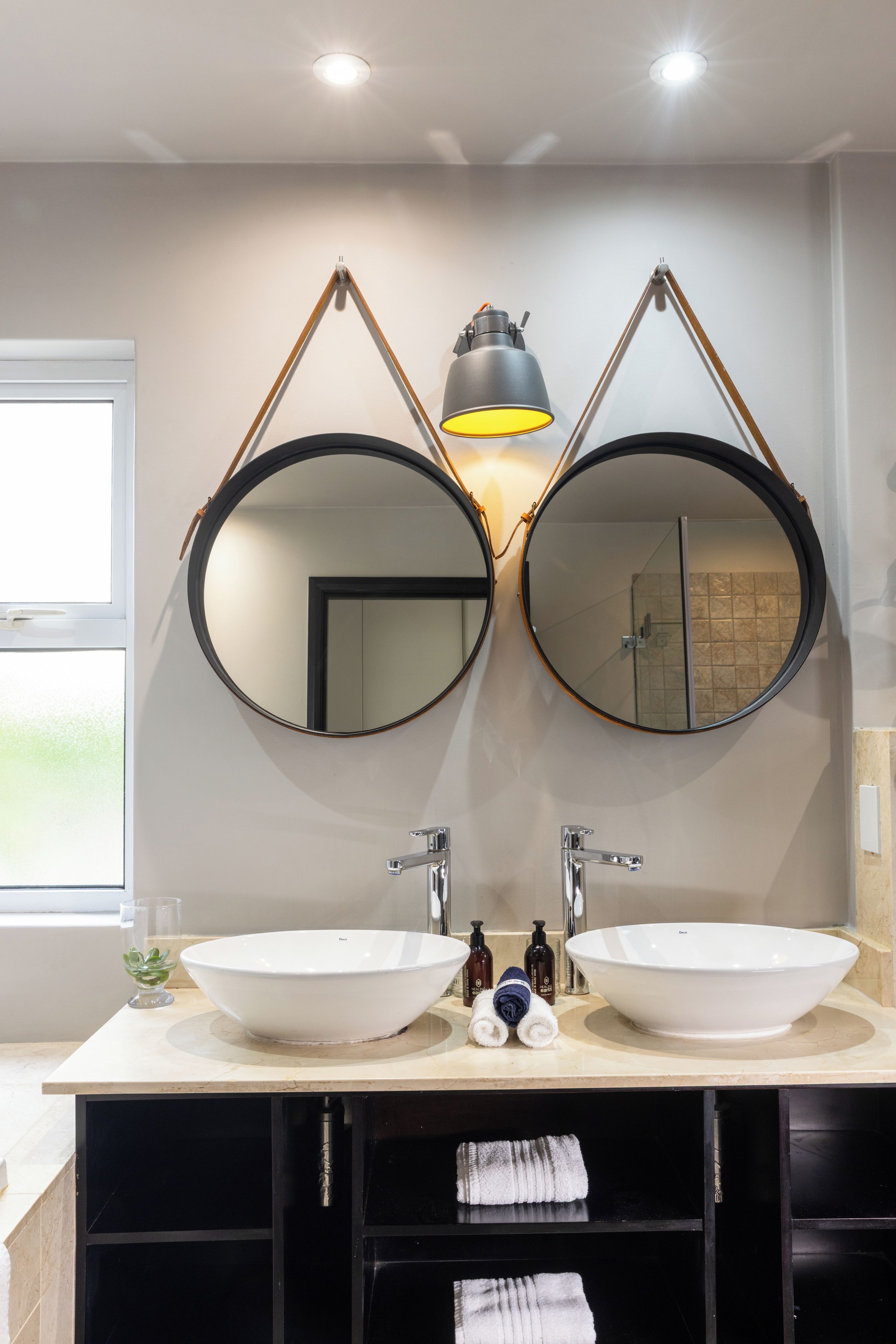A bathroom with two round mirrors, a white sink, and a towel rack.