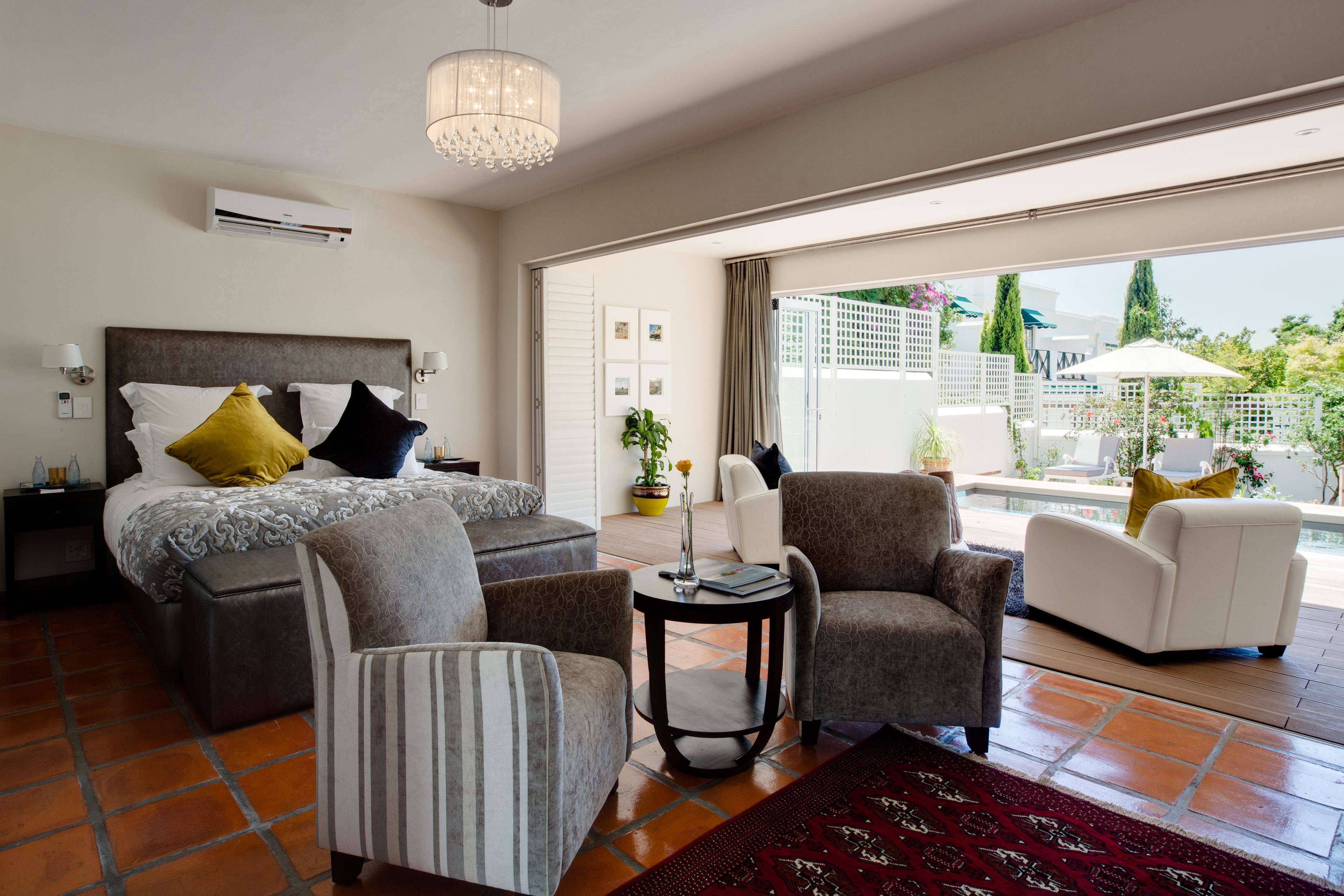 A hotel room with a bed, two armchairs, a small table, and a view of the outdoor area.