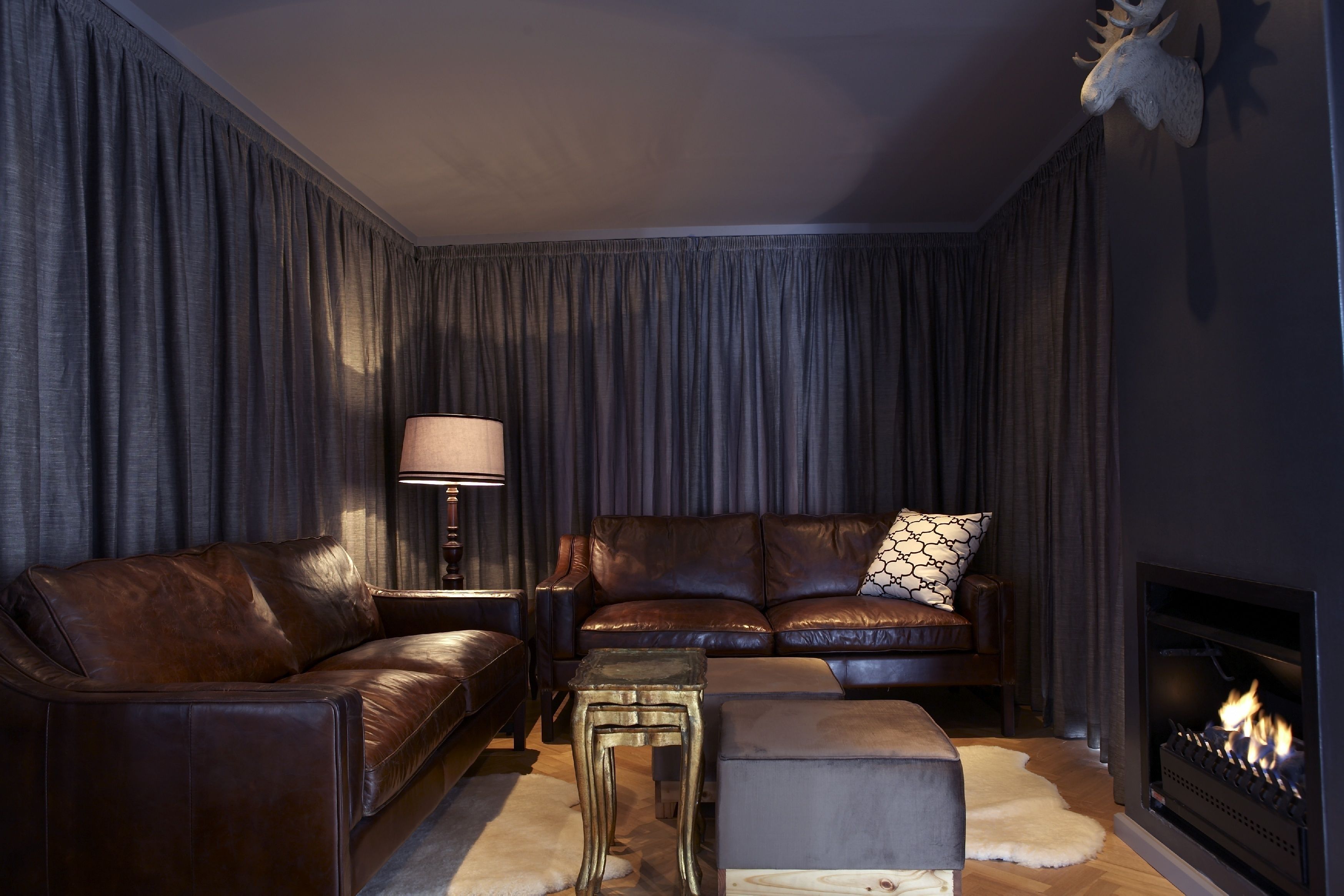 A cozy living room with a leather sofa, a matching ottoman, a side table with a lamp, and a fireplace.