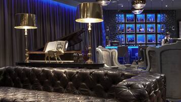 A luxurious lounge area with a grand piano, plush leather sofas, and a bar with blue lighting.