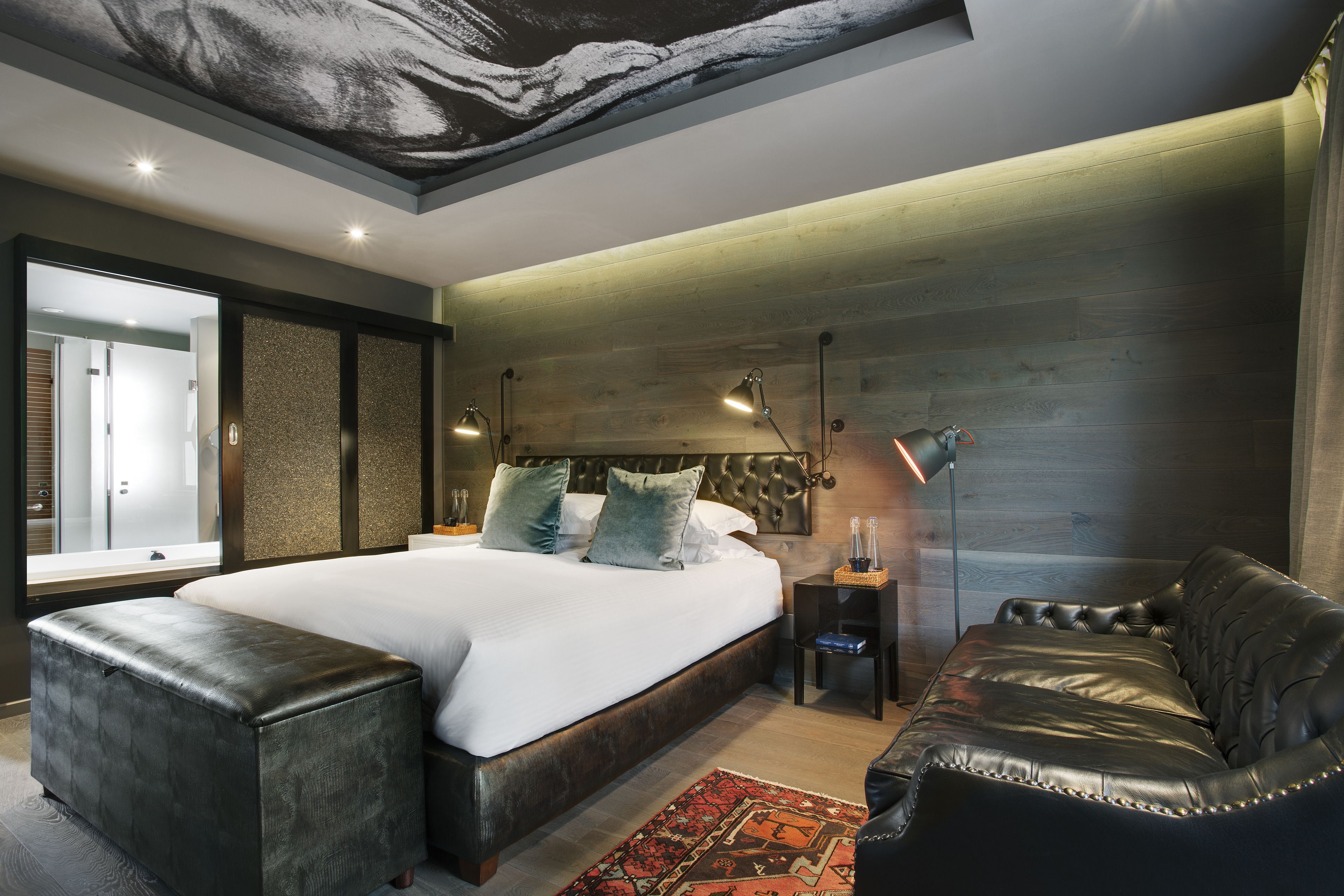 Un dormitorio moderno con una cama grande, un sofá de cuero y un mural único en el techo.