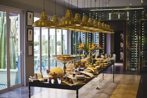 A buffet table with various food items and a pig-shaped centerpiece, set in a room with large windows and hanging gold pendant lights. - Majeka House Boutique Hotel (Stellenbosch)